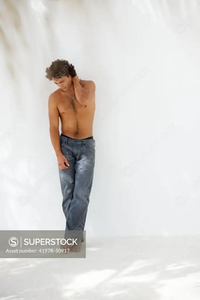 Full-length of a sexy young man wearing jeans but no shirt posing ahainst a white wall