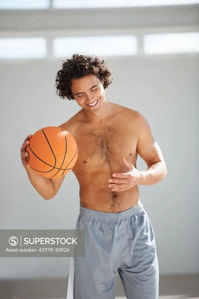 Gorgeous young man wearing no shirt holding a basketball while smiling happily