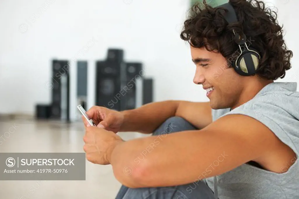 Handsome young man listening to music on his mp3 player with his stereo system in the background