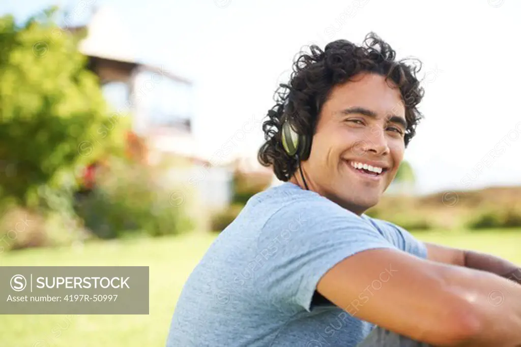Gorgeous young man listening to music on his headphones,  smiling at you while outdoors