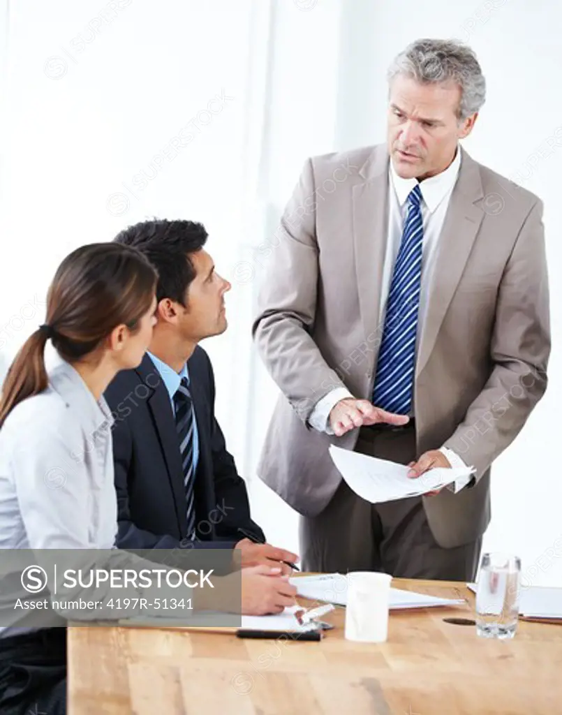 Businessman sternly addressing to young associates sitting at a boardroom table