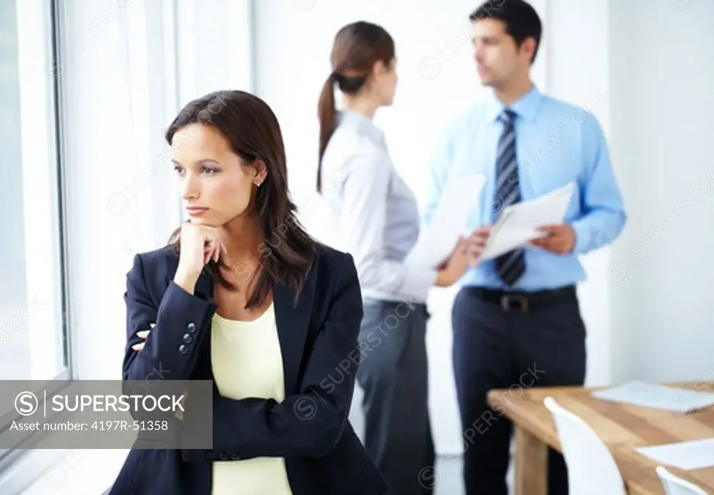 Beautiful businesswoman gazing out of the window pensively with two people in the background