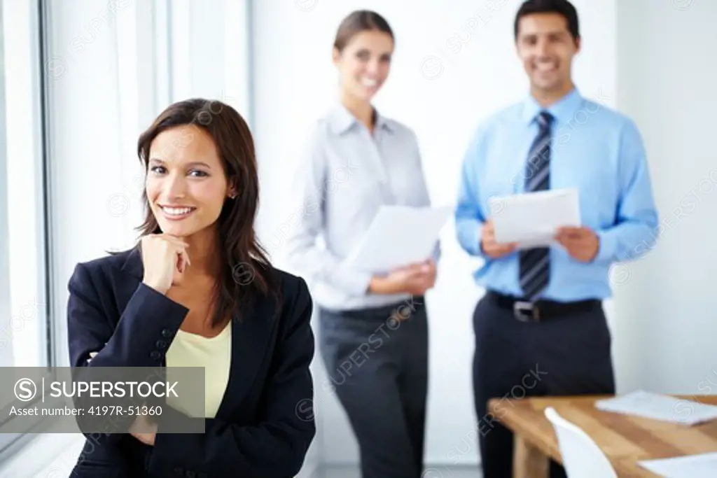 Happy young businesswoman smiling at the camera with two co-workers standing in the background