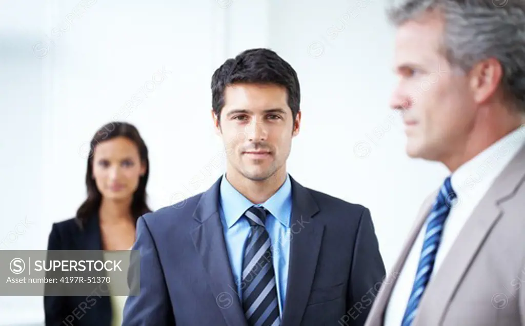 Succesfull young businessman looking at the camera wth co-workers in the foreground and background