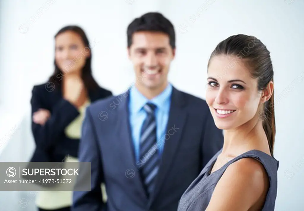 Happy young businesswoman smiling at the camera with two co-workers standing in the background