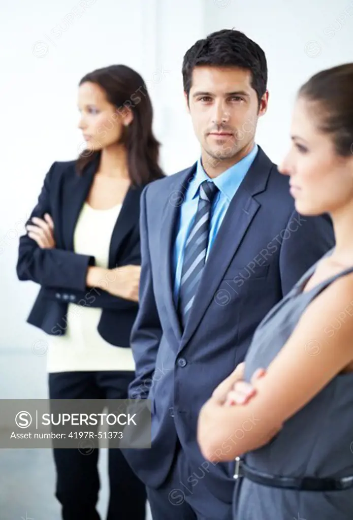 Attractive young businessman looking straight at the camera with female co-workers at his side