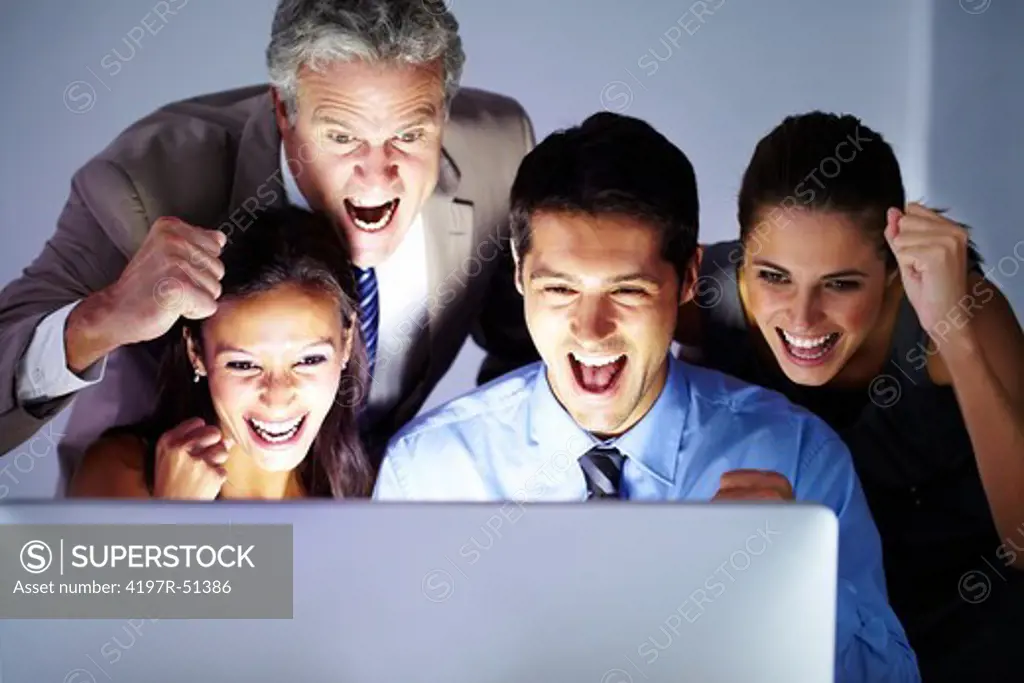 Group of co-workers huddled around a screen smiling with their fists in the air in an expression of victory