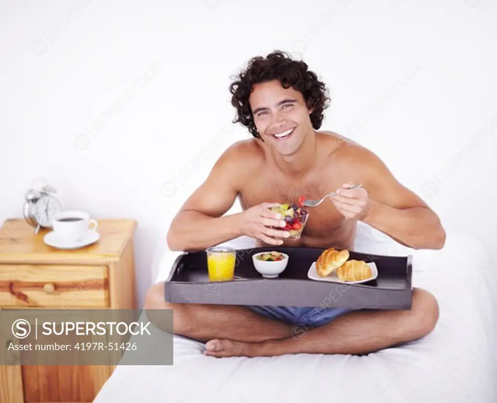 Portrait of a happy healthy young man eating a wholesome breakfast on his bed