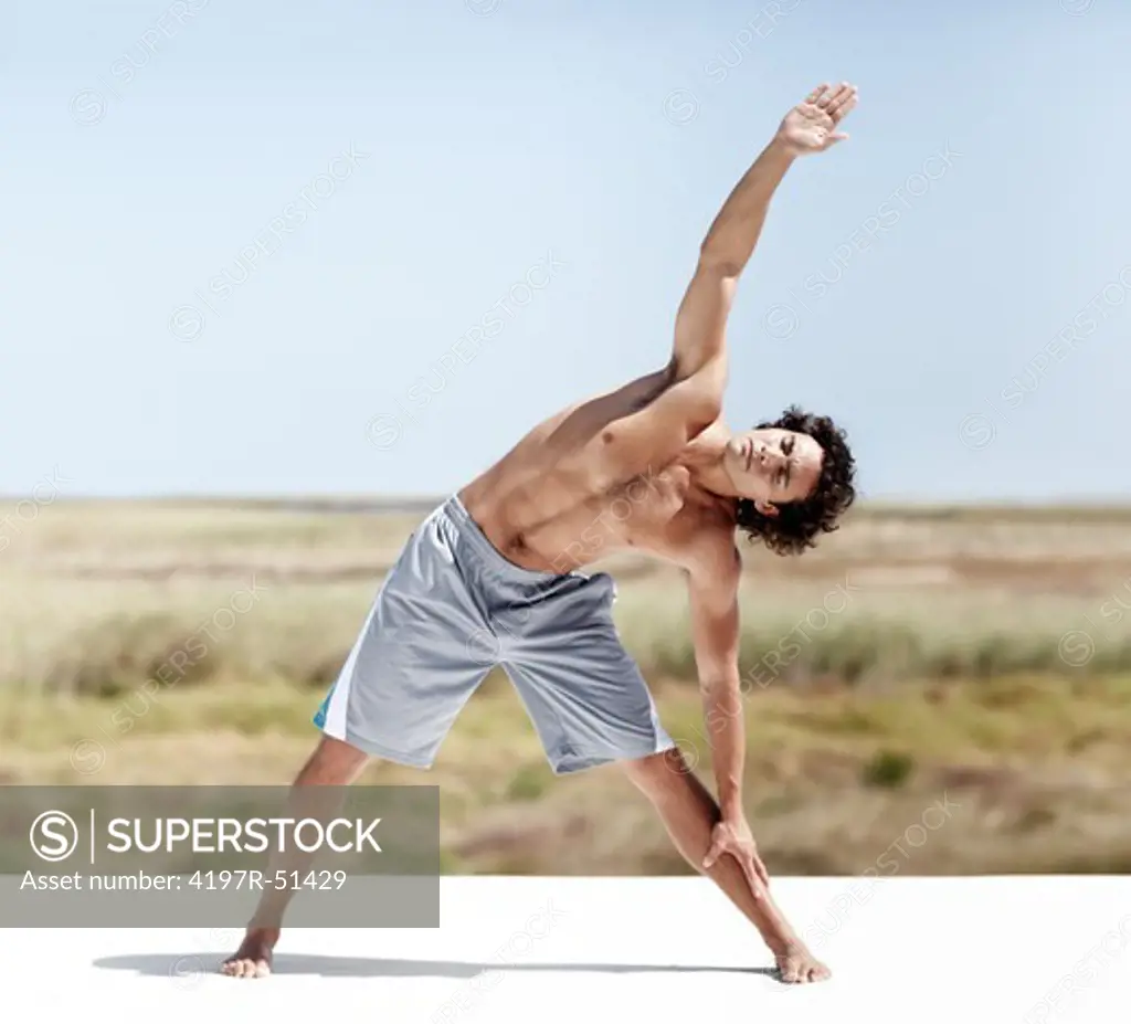A healthy young man standing in the triangle yoga pose with his eyes closed