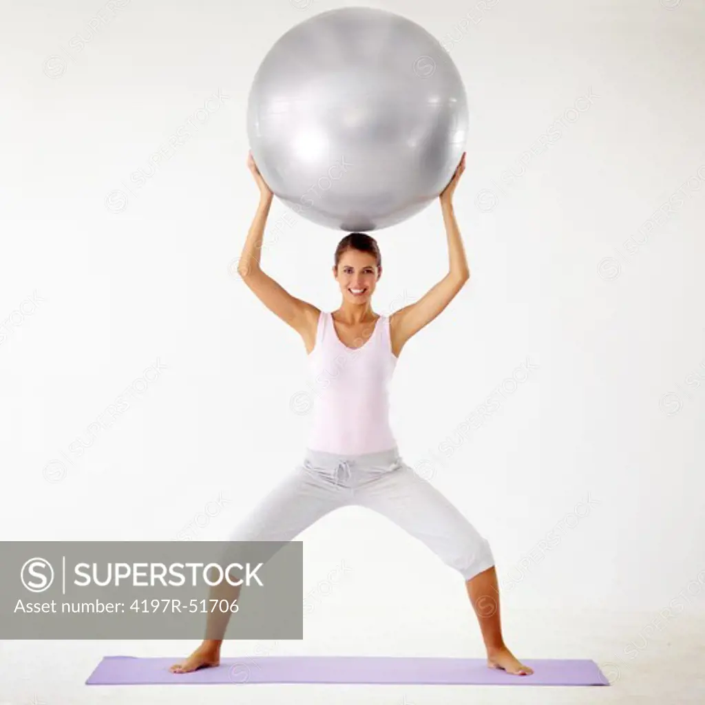 Young woman holding a gym ball above her head while squatting - Isolated on white