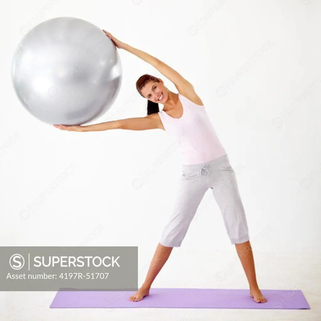 Young woman holding a yoga ball and stretching to the side - Isolated on white