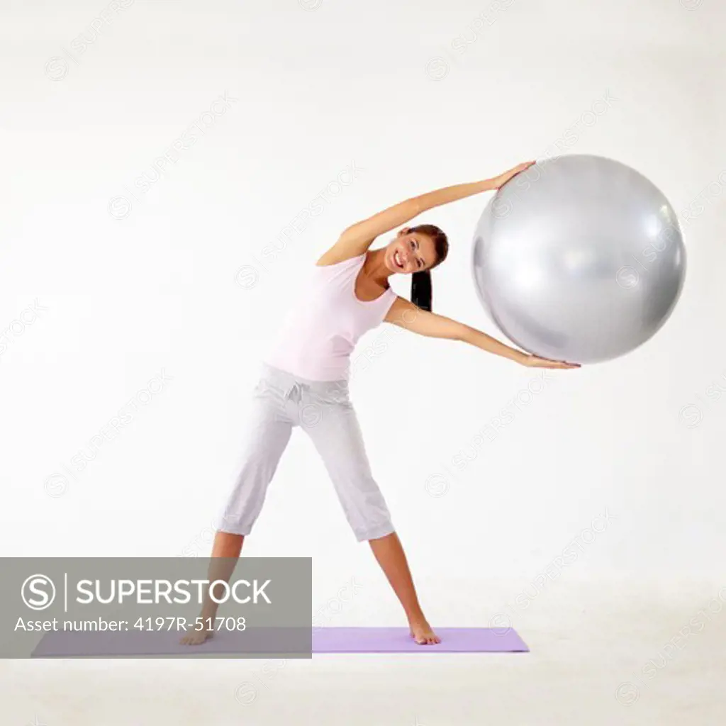 Young woman holding a swiss ball and stretching to the side - Isolated on white