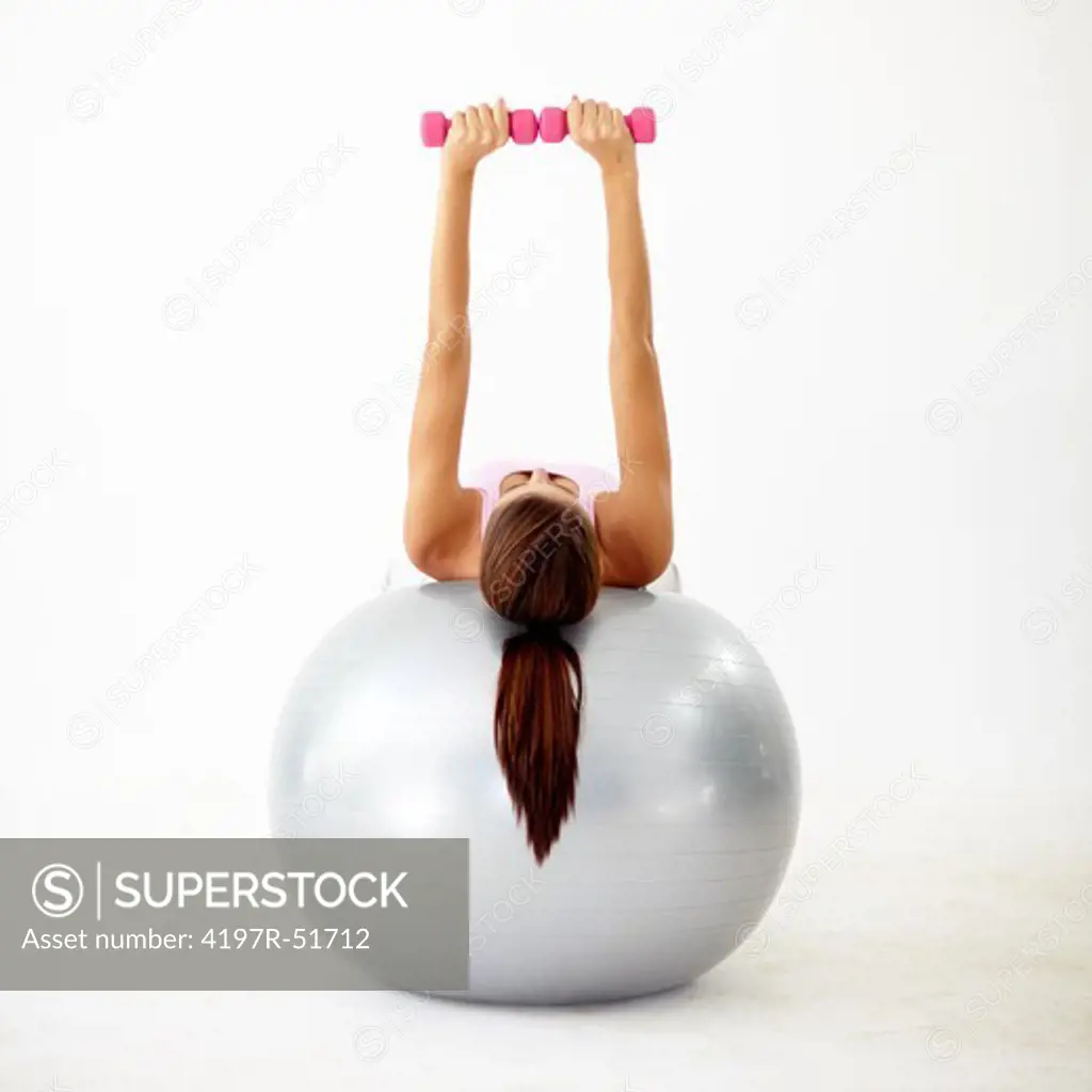 Rear view of a young woman doing dumbbell presses on a swiss ball