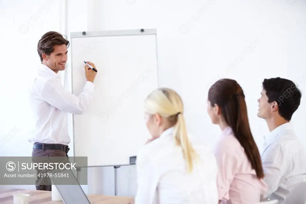 Young businessman giving a presentation using a whiteboard while his colleagues look on