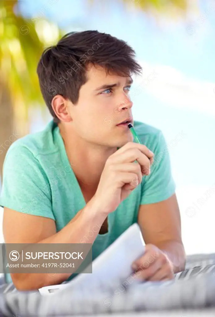 Young man thinking about what to write while sitting outdoors
