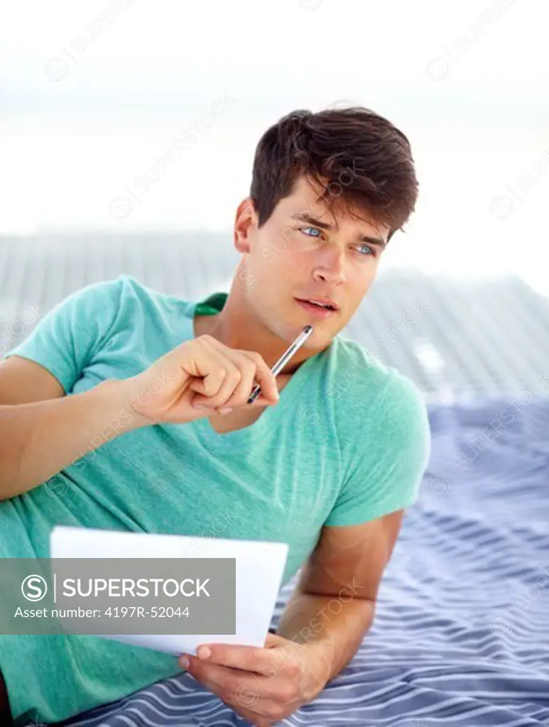 Young man brainstorming holding a pen and sheets of paper in his hands