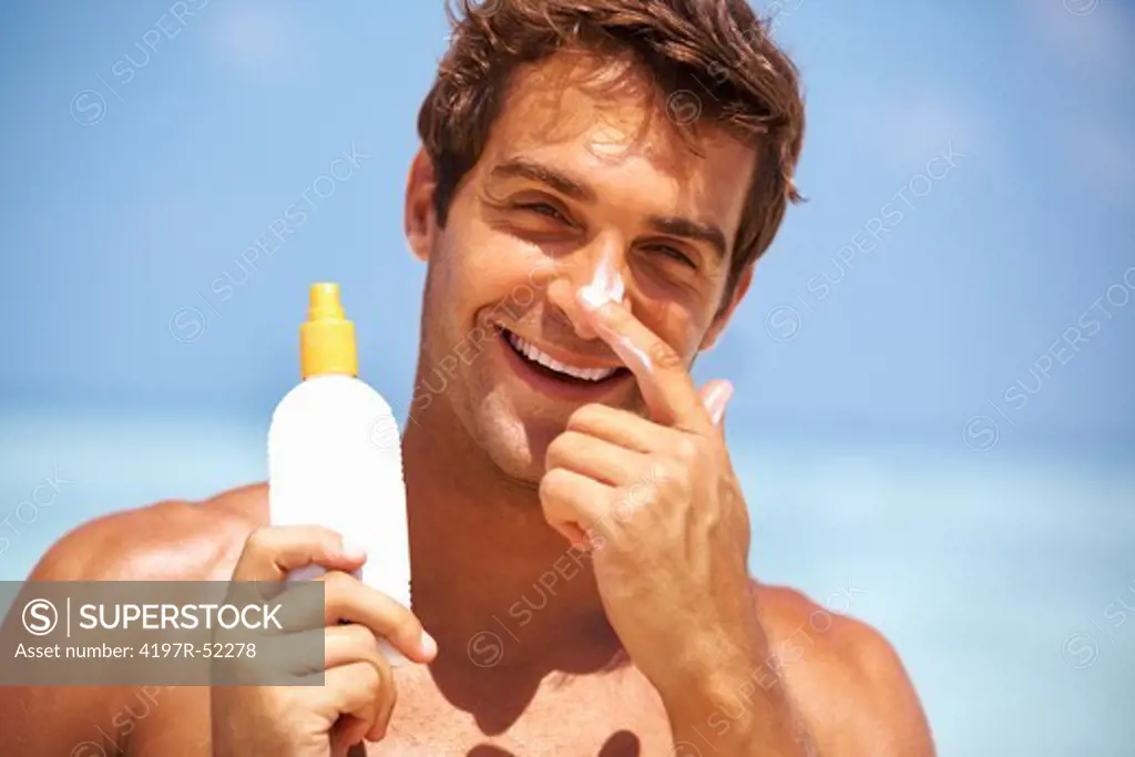Closeup of smart young man applying sunscreen lotion on his face