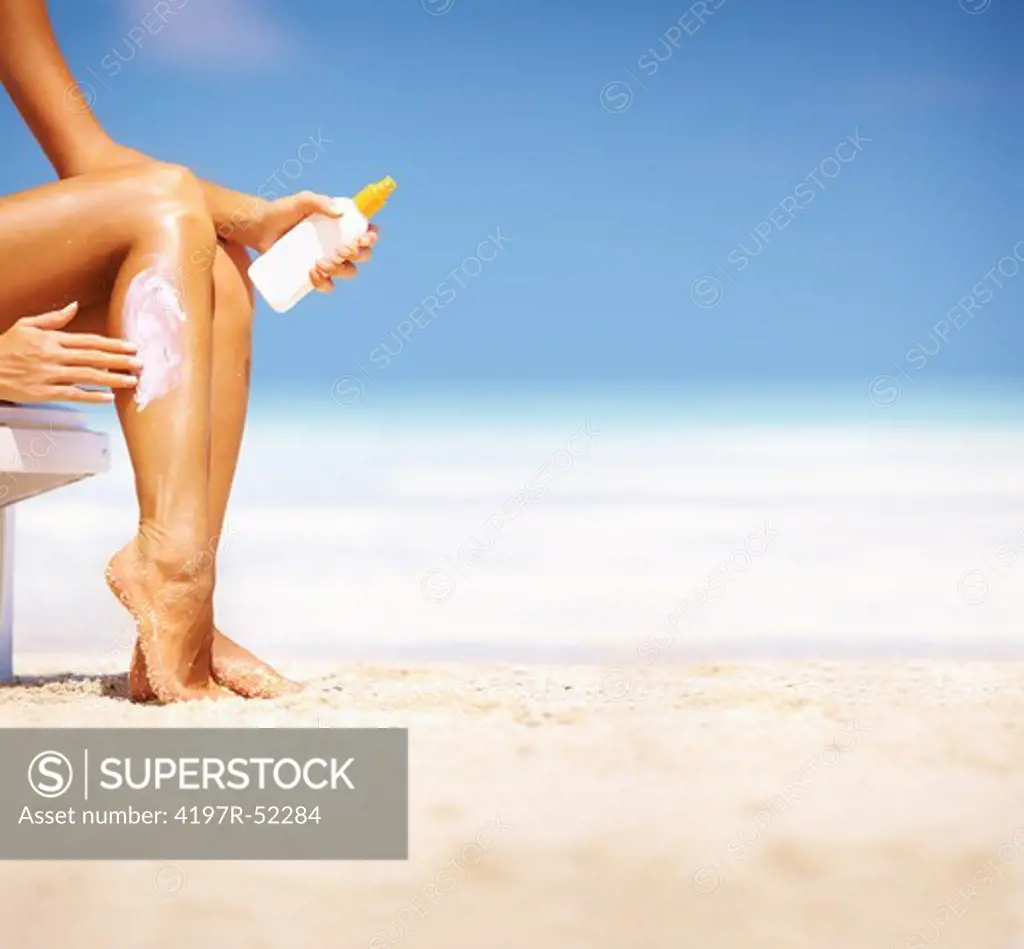 Portrait of woman applying sunscreen lotion on her sexy legs at beach