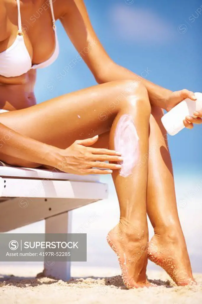 Portrait of young woman in bikini applying sunscreen lotion on legs
