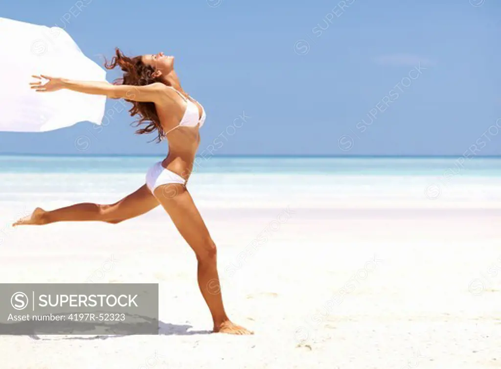Portrait of carefree young woman running with white sarong at beach