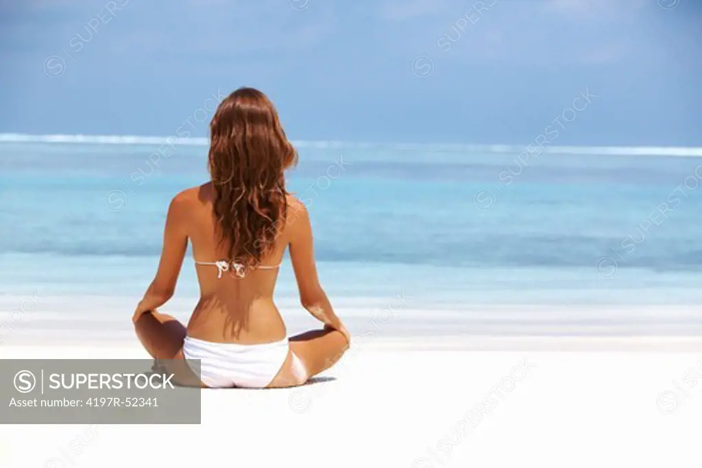 Portrait of young woman meditating in lotus position at beach