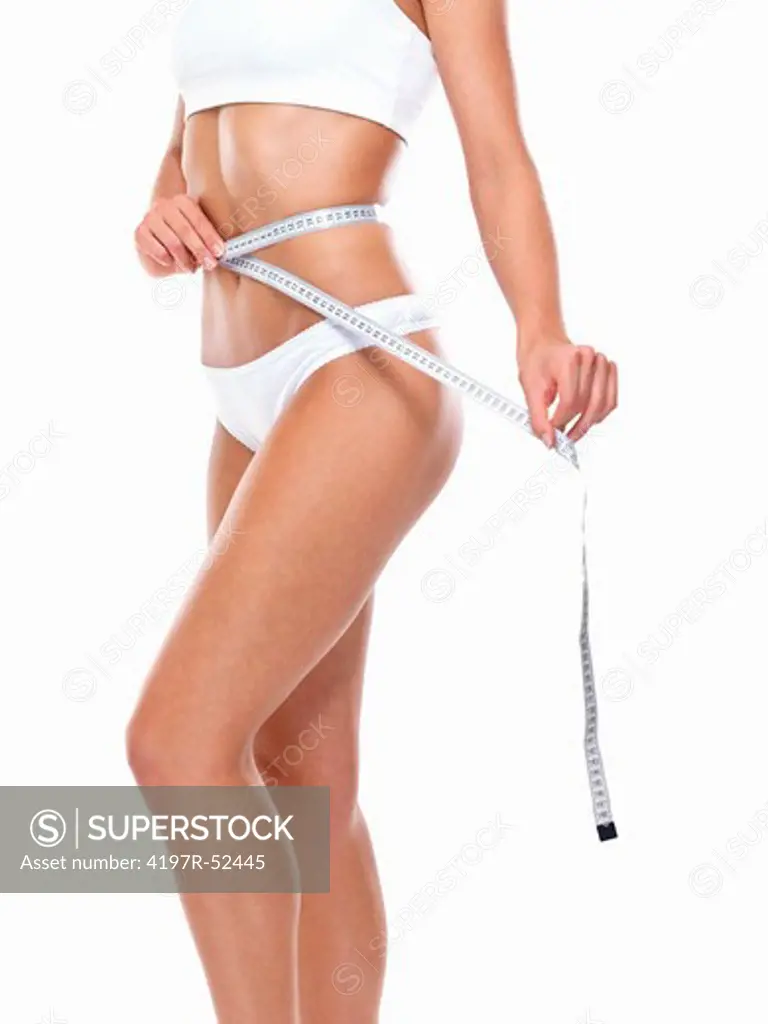 Mid section of young woman measuring belly over white background