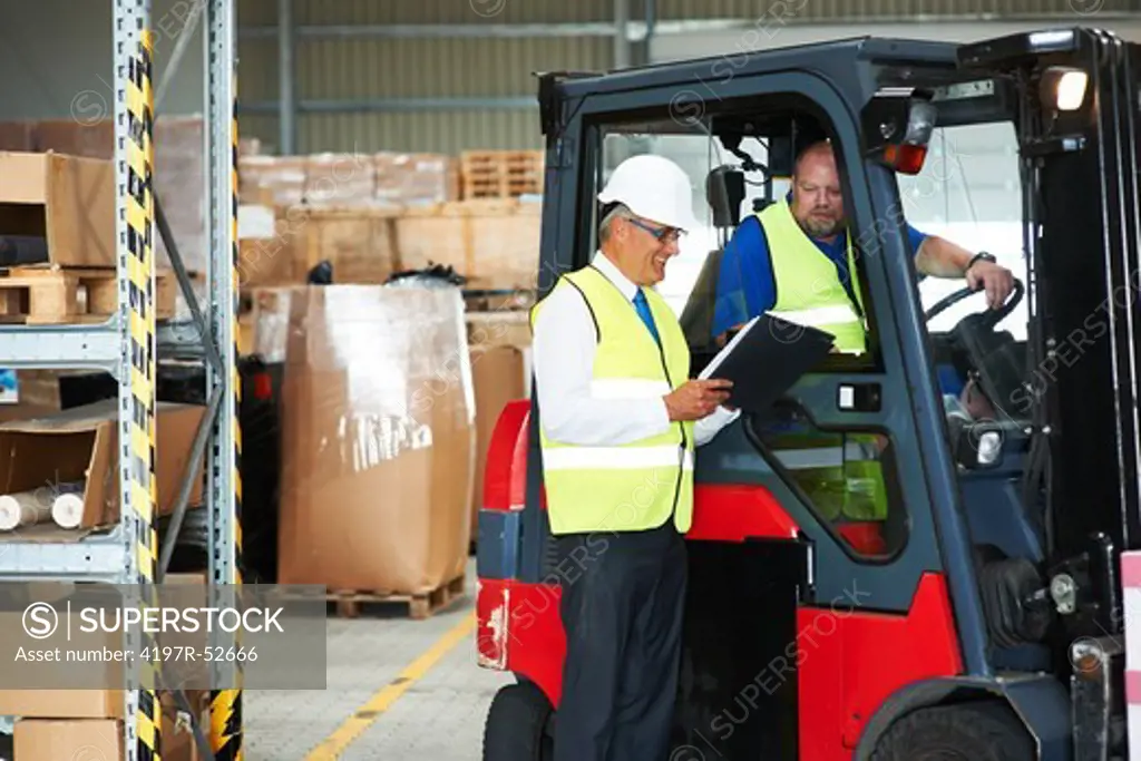 Foreman at a warehouse giving instructions to an employee in forklift