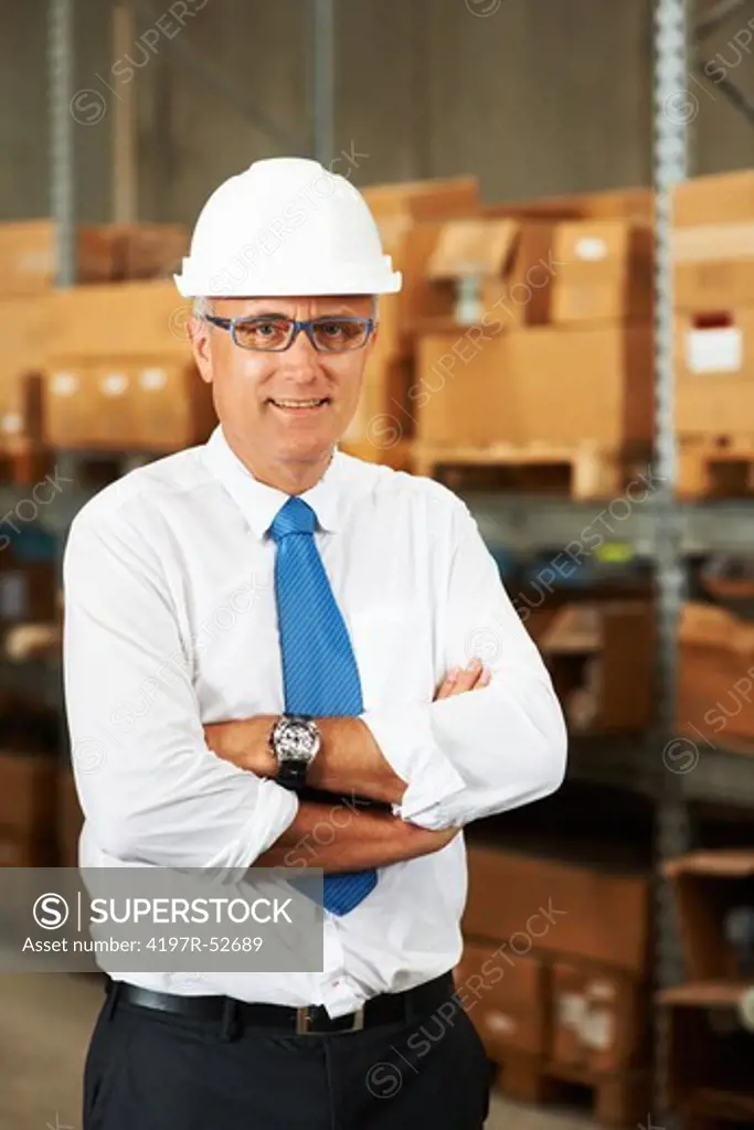 Portrait of smiling male supervisor crossing his arms in front of shelved boxes of stock