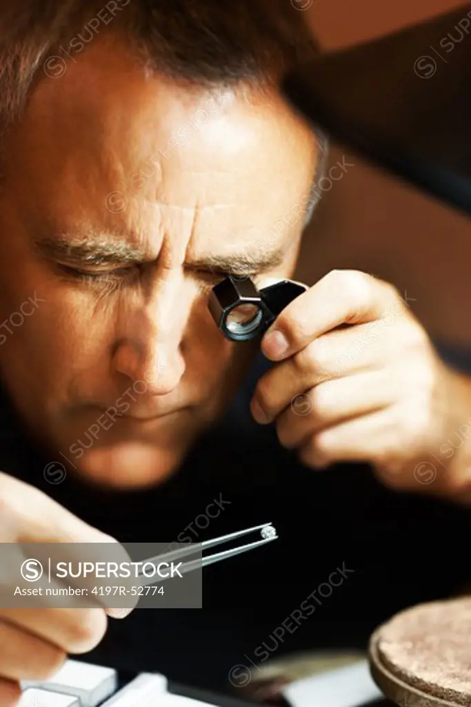 Male jeweler Looking through a magnifier to check for flaws in a diamond