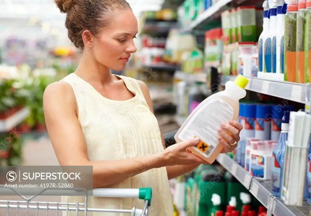 Attractive ethnic woman with trolley holding bottle product and looking at it