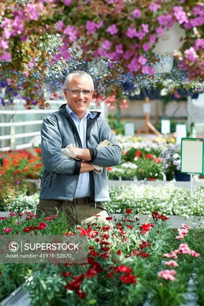 Mature caucasian male florist with folded arms smiling surrounded by variety of flowers