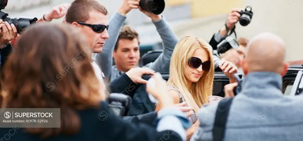 Celebrity star being photographed by the paparazzi while getting into a car