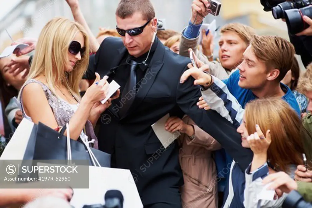 Pretty young star signing autographs while her bodyguard holds back the public