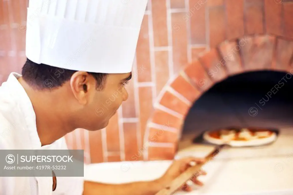 Young chef putting pizza in wood fire oven in restaurant
