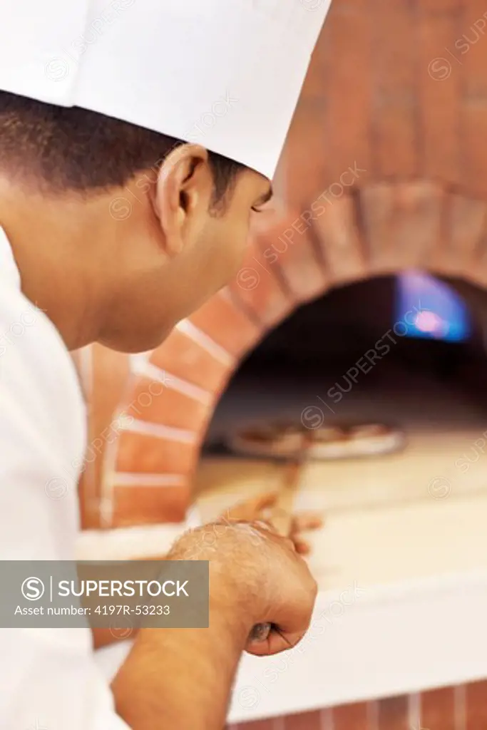 Closeup of young cook placing fresh pizza in wood fire oven for baking in restaurant