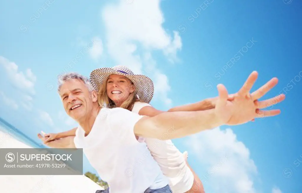Portrait of carefree mature couple having piggyback ride together on beach