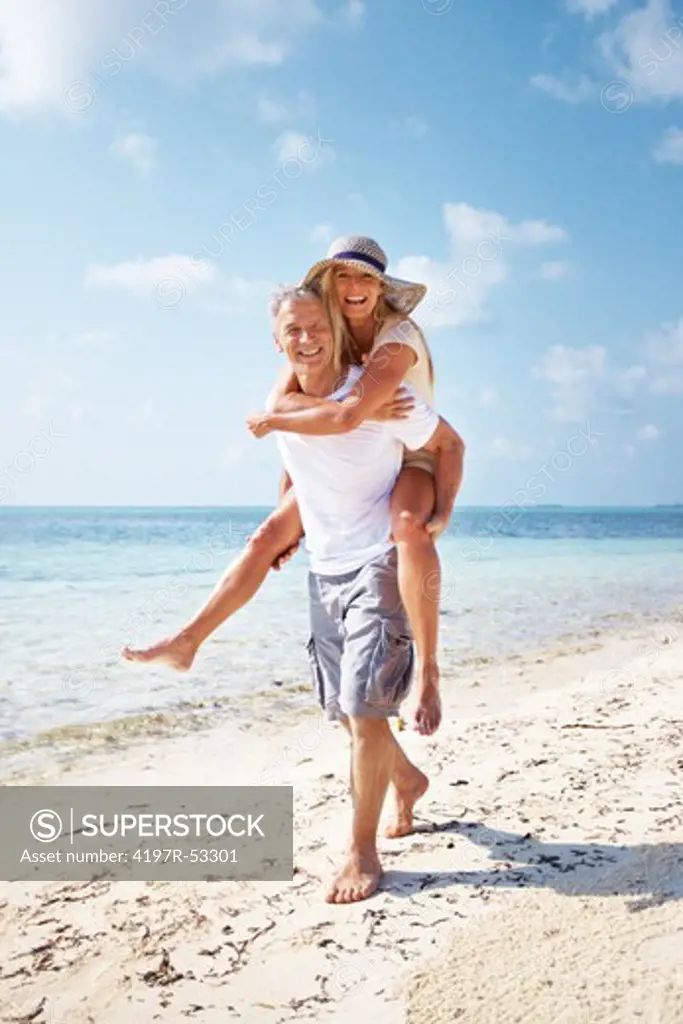 Full length of happy mature couple enjoying while piggyback ride on beach