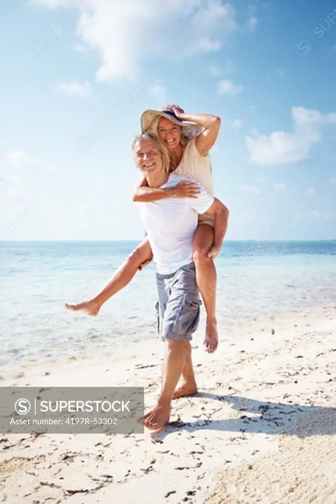 Full length of carefree couple having piggy back ride together on beach