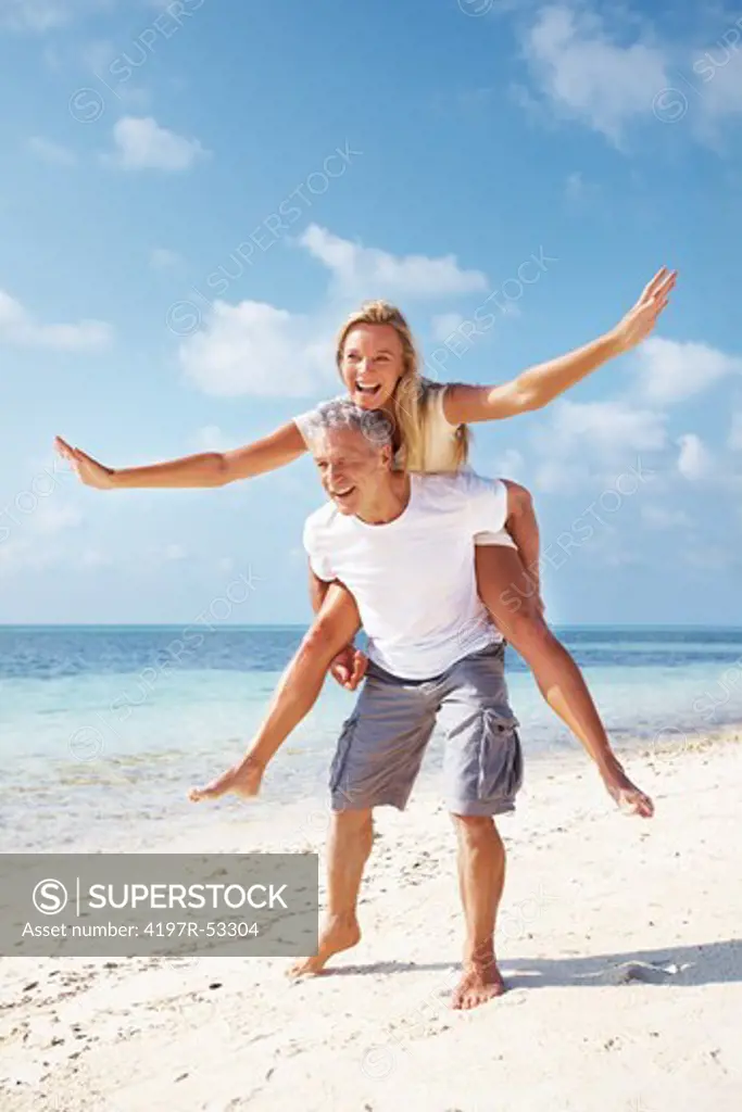 Full length of happy mature couple having piggyback ride on beach
