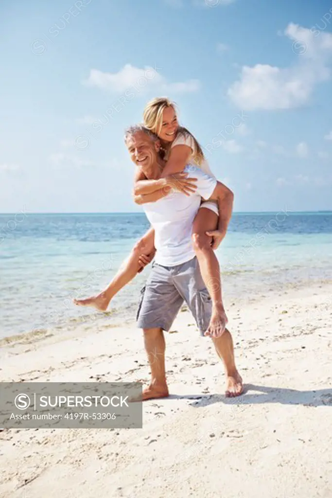 Full length of cheerful mature couple having piggyback ride together on beach