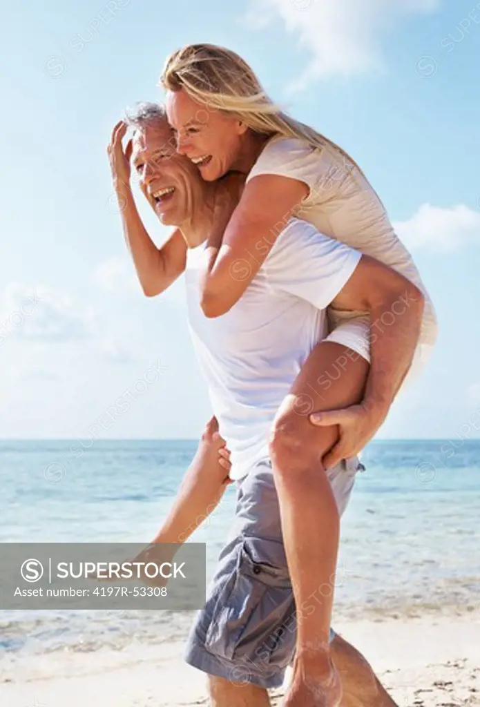 Portrait of happy mature man walking while carrying woman on beach