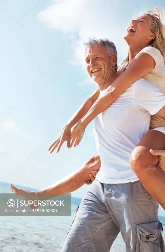 Portrait of cheerful mature couple enjoying piggyback ride together on beach