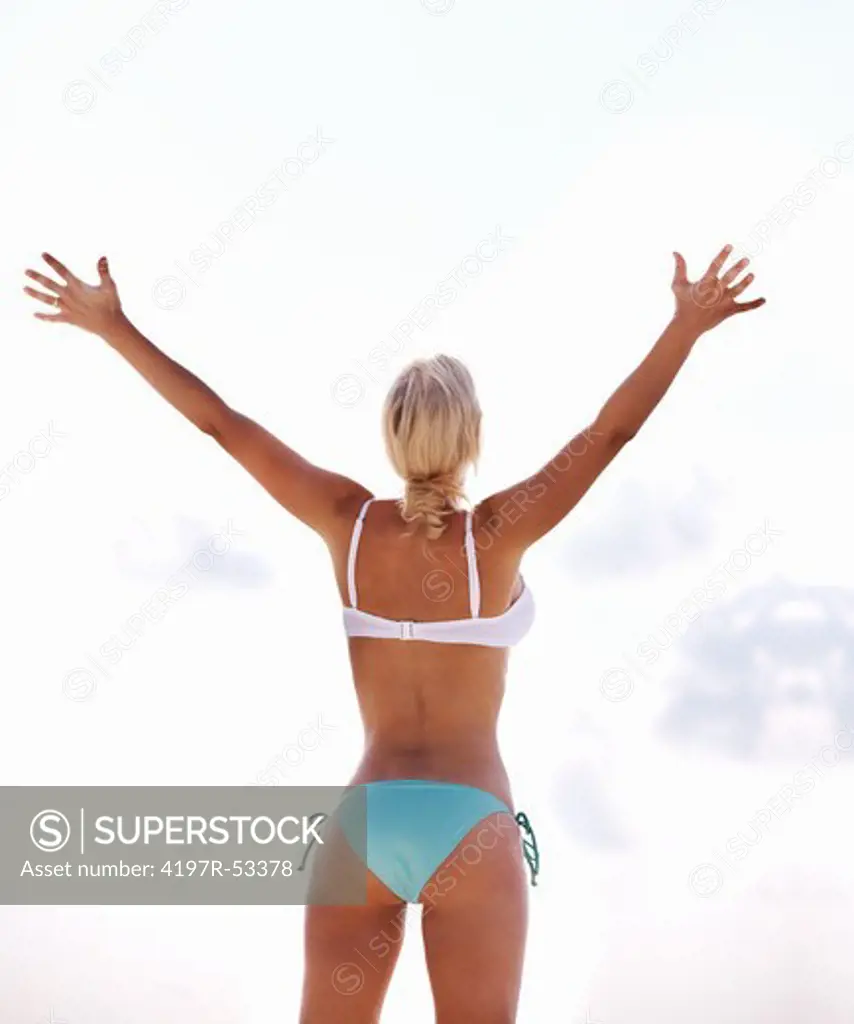 Rear view of fit woman standing with hands raised on the beach