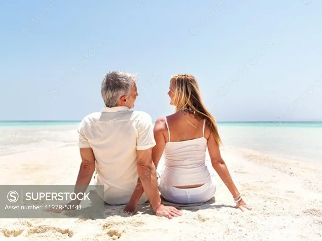 Rear view of romantic mature couple sitting relaxed at the beach looking each other