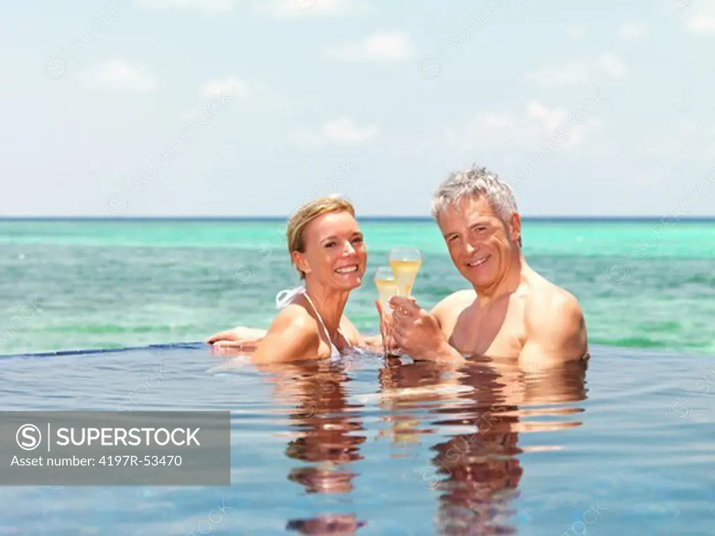 Portrait of romantic mature couple in pool with champagne by the sea