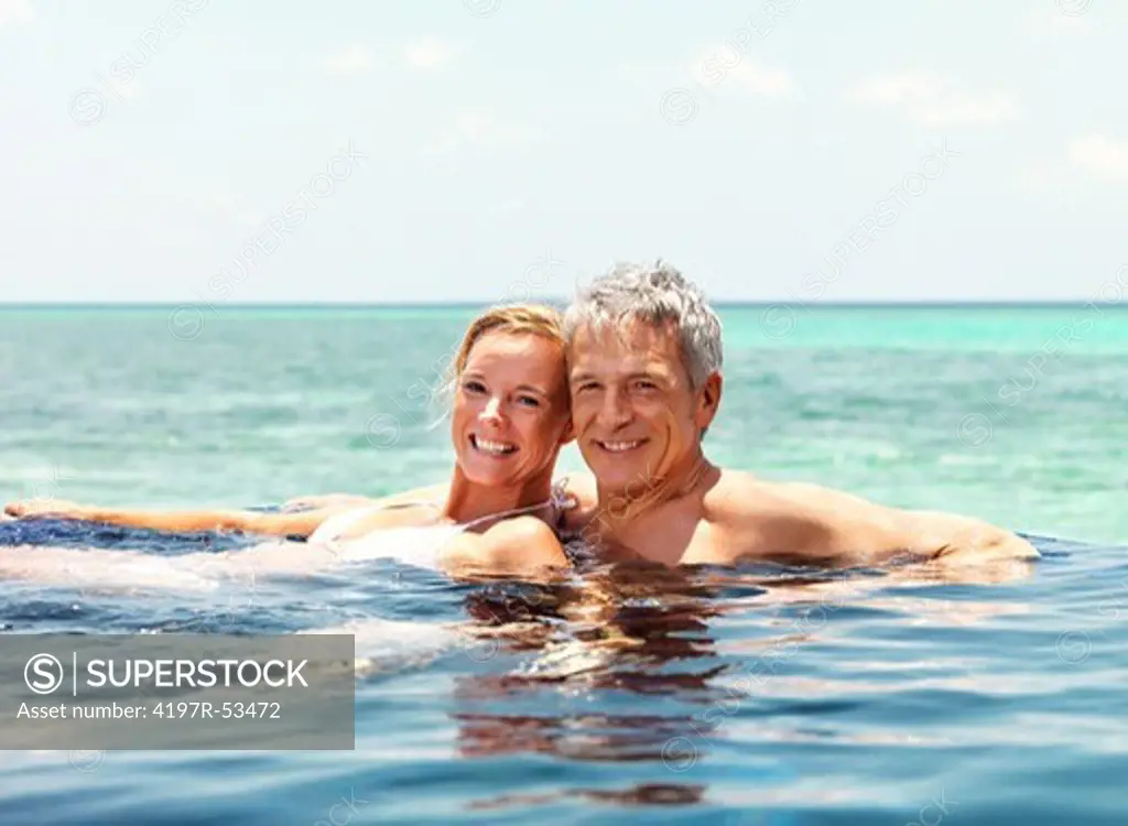 Loving mature couple enjoying their vacation in a swimming pool by the seaside