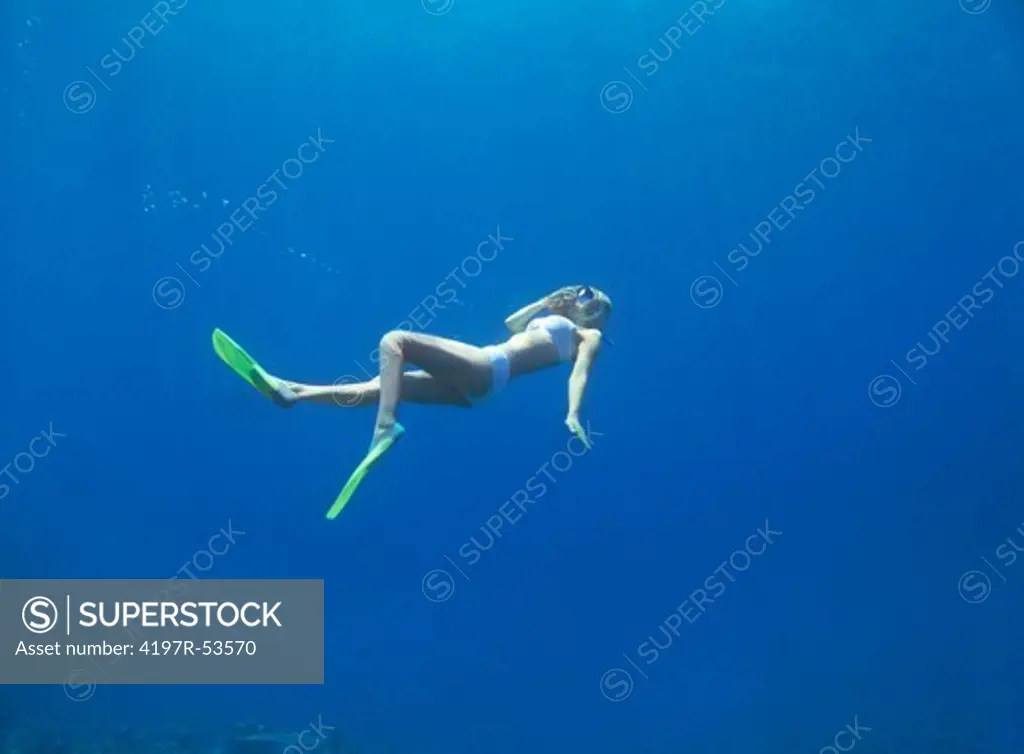 Young woman in snorkeling gear swimming through infinite blue water - copyspace