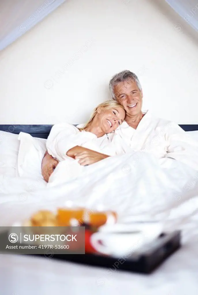 Portrait of a happy mature couple on bed with breakfast in front