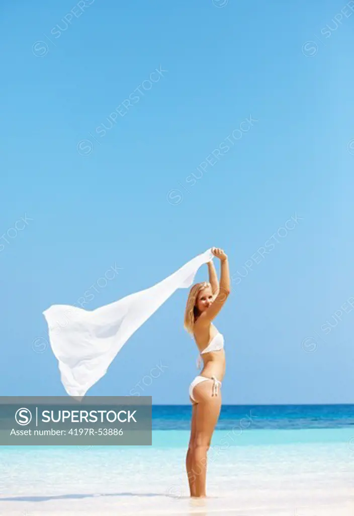 Attractive young blond holding a sarong against the blue horizon