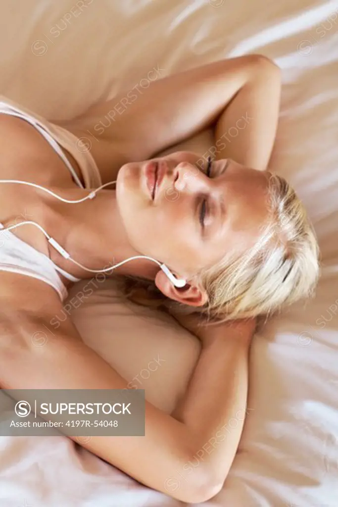 Relaxed young girl lying on bed and listening to music with earphones